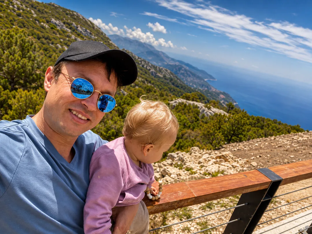 Selfie of Falko holding his child high above a coastline with a view of the sea