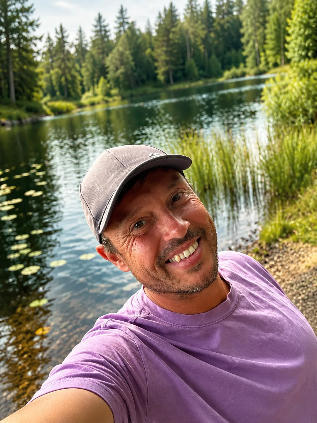 Falko smiles at the camera, with a quiet lake, water lilies, and forest behind him