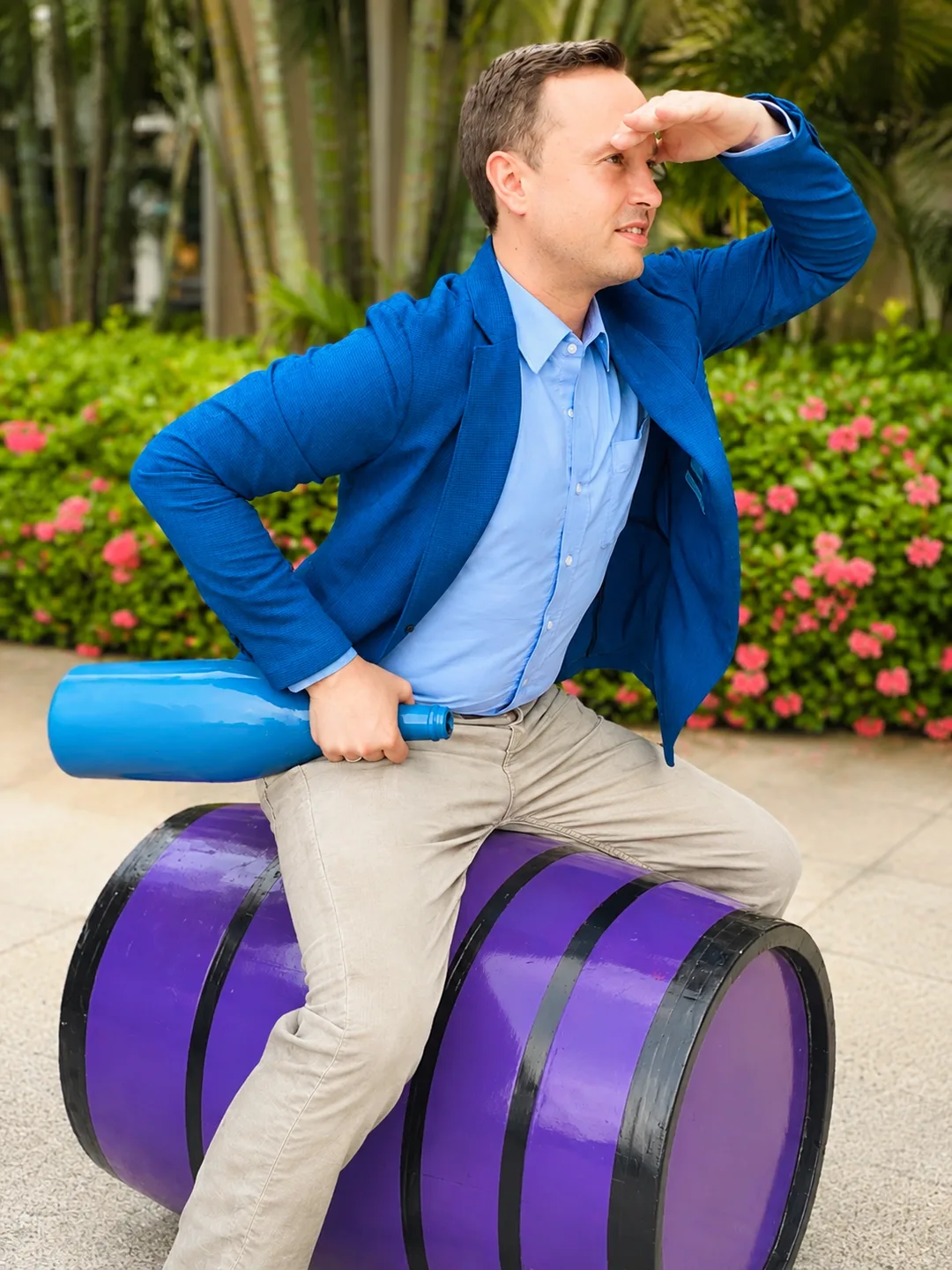 Falko in a blue suit sits on a purple wine barrel with a blue bottle, looking thoughtfully into the distance